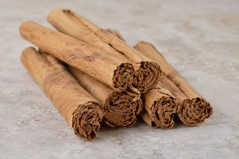 Golden-brown Ceylon cinnamon quills stacked on pale stone, with layered, frayed ends facing the camera.