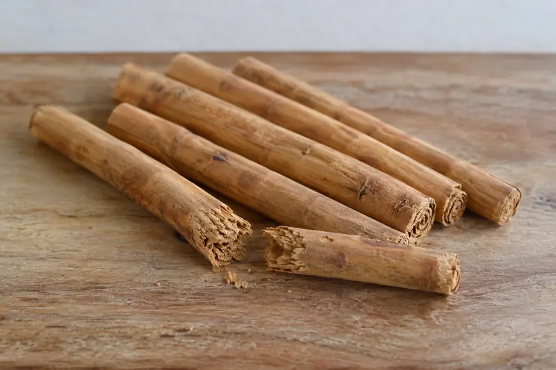 Golden-brown Ceylon cinnamon quills on a wooden board, with one broken open to reveal its fine, crumbly layers.