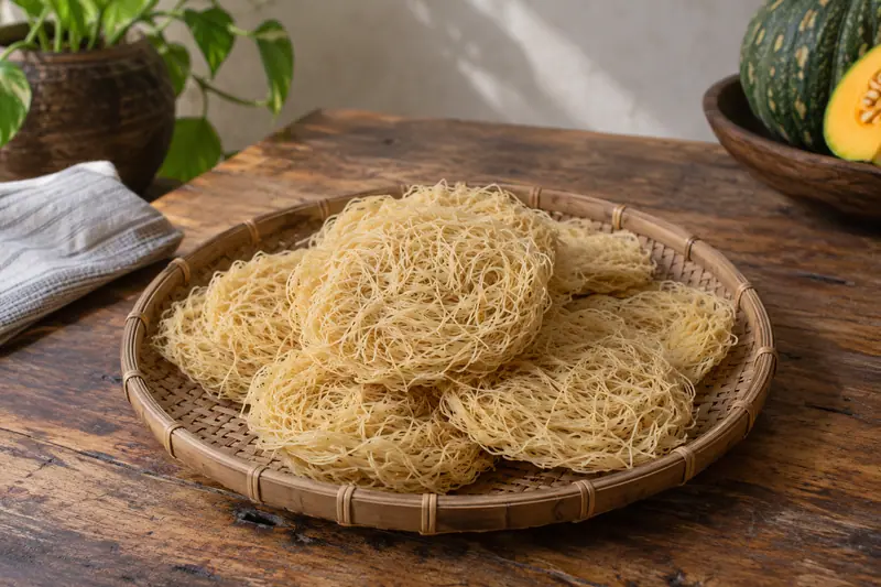 Pale yellow dried pumpkin string hopper nests overlap on a woven cane tray on a rustic wooden table.
