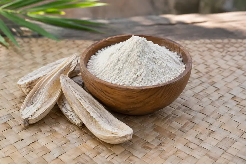 Pale odiyal flour heaped in a wooden bowl beside split dried palmyrah tubers on a woven palm leaf mat.
